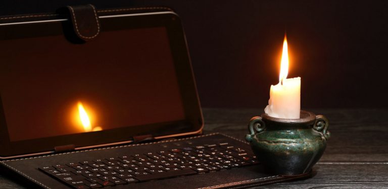 49927316 - blackout concept. lighting candle near laptop with dark empty screen