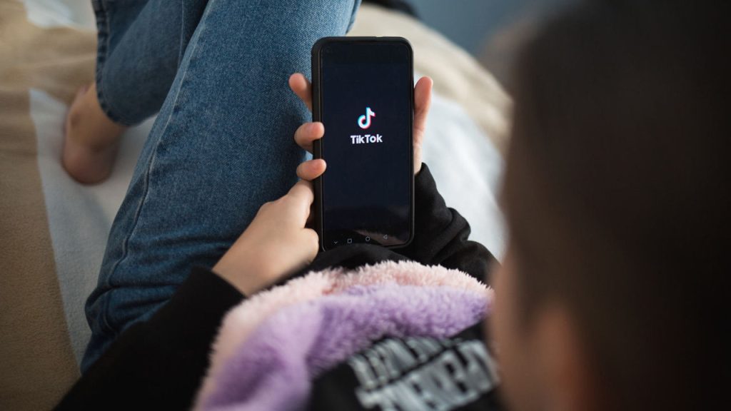 Nizhny Novgorod, Russia - October 03 2020: child with phone in his hands is lying at home on bed. Social Media tiktok is loaded on screen